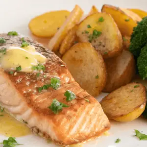 A beautifully plated dish of lemon butter salmon garnished with parsley, accompanied by crispy golden potatoes and bright green broccoli, arranged on a white plate with a light, elegant background.